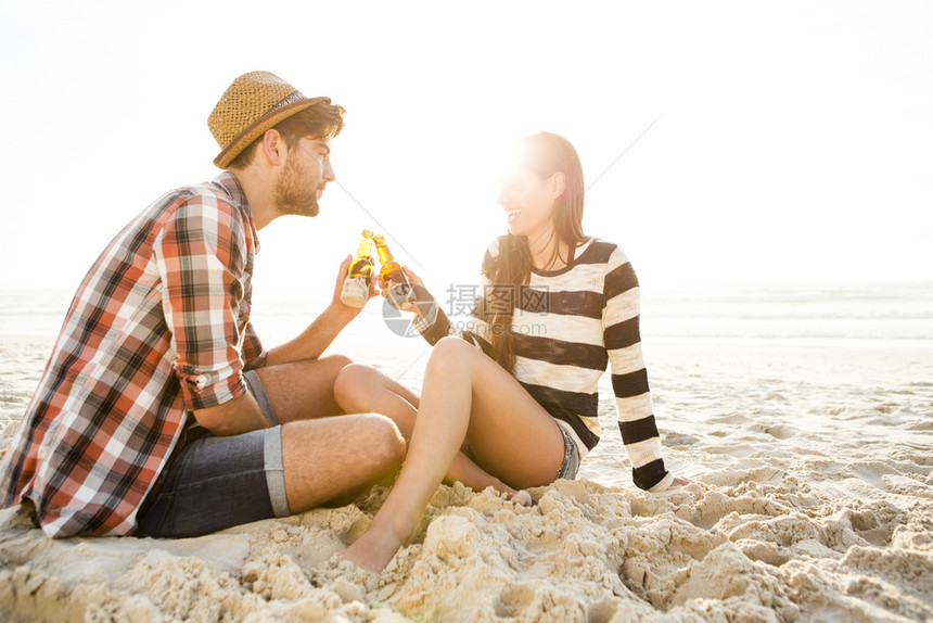 美丽的年轻在海滩上玩乐笑和喝啤酒的年轻夫妇干杯图片