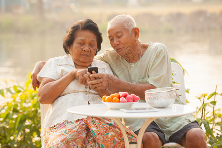 年长的在户外背景使用手机的快乐亚洲老夫妇情侣家技术图片