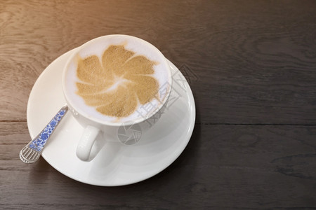 泡沫黑色木制桌椅上白陶瓷杯中的热卡布奇诺拿铁艺术表面有照明灯喝咖啡图片