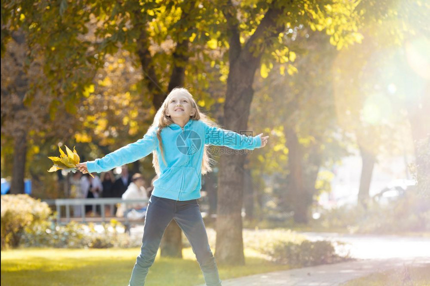 女孩举起她的手臂享受公园的日落秋天树叶女图片