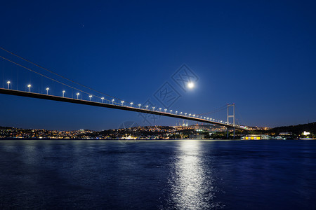 夜晚旅行河博斯普鲁海峡大桥夜间被灯光和月亮照博斯普鲁海峡大桥到岸明亮的月下有灯火通明的房屋土耳其伊斯坦布尔博普鲁海峡大桥夜间被灯背景图片