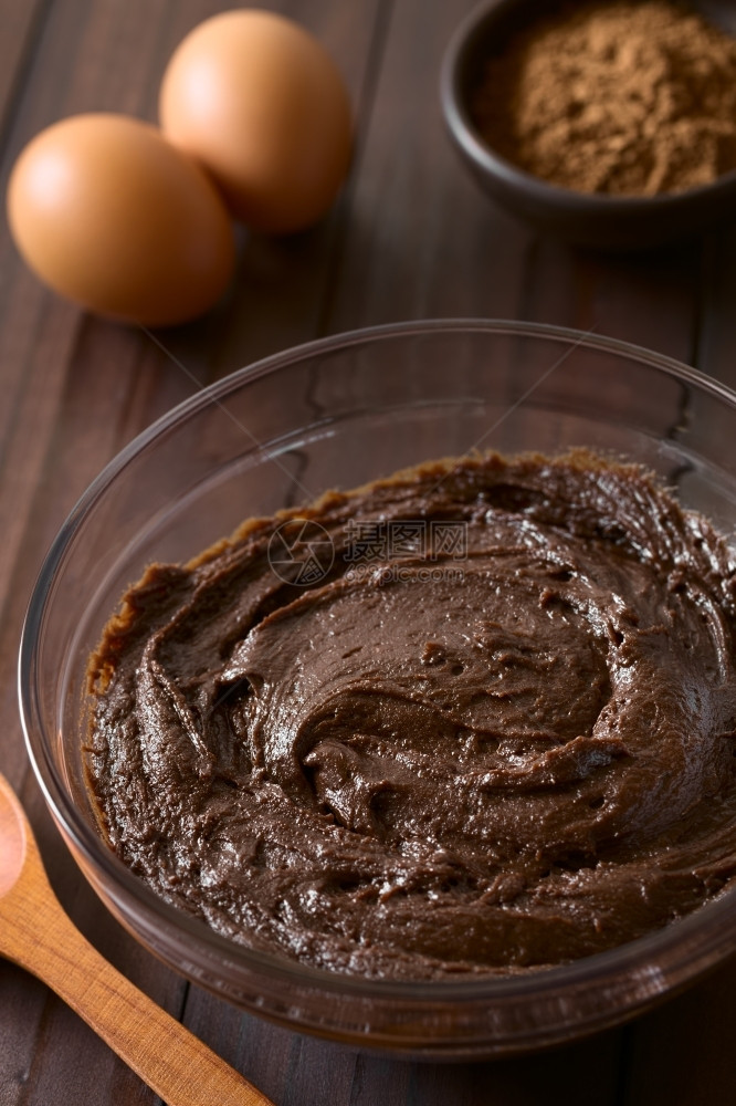 混合粉末自制基本土布朗尼巧克力蛋糕或饼干面团放在玻璃碗中后面有可粉和鸡蛋在黑木上拍照面有天然光照图象聚焦点三分之一图片