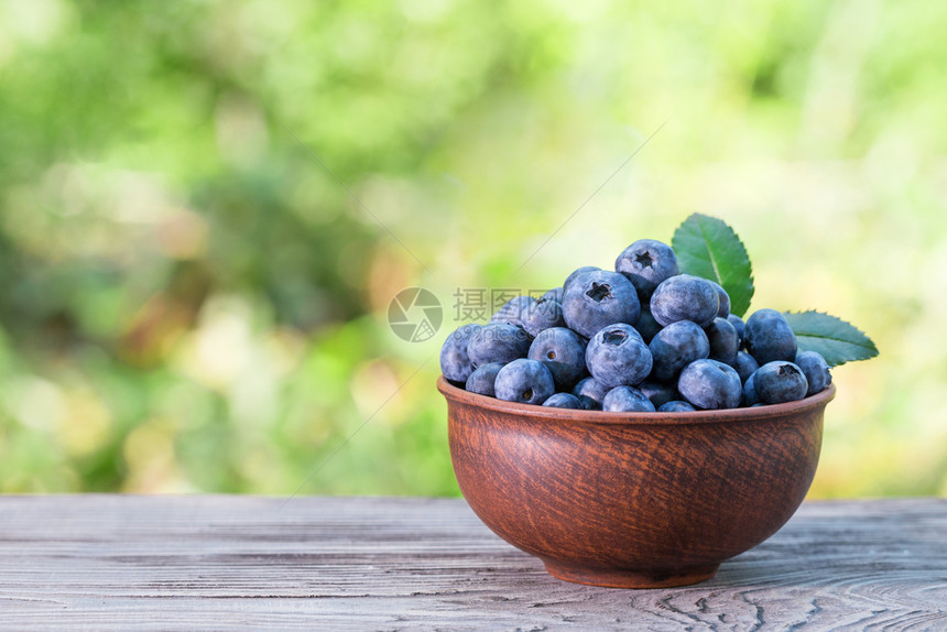 蓝莓在木制桌边的粘土碗上绿色天然背景夏月保持生命自然产品和收获概念在木制桌子上的粘土碗收成有机的素食主义者图片