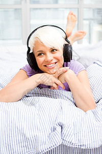 屋成人金发女郎在床上用耳机监听MusxAic快乐的图片