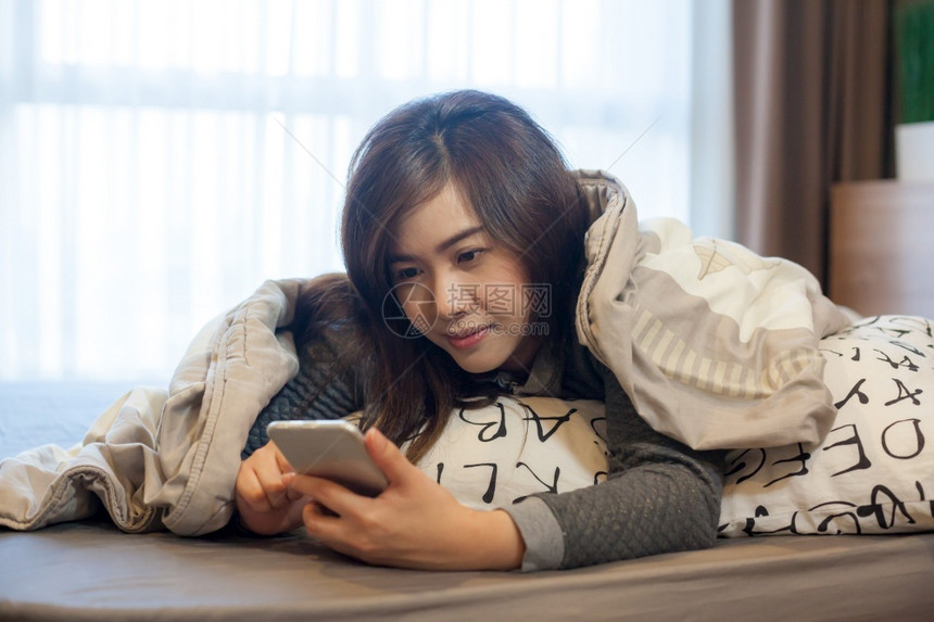 漂亮的在家里床上用智能手机躺在床上的快乐亚洲年轻女子士闲暇图片