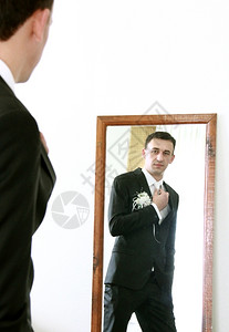 衬衫时髦的严肃长得很英俊新郎照着镜子看他的领带图片