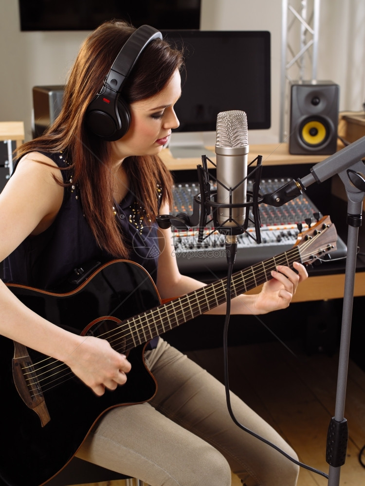 照片中一位美丽的黑发女在录音室里演唱一首响吉他歌唱成一个大隔膜麦克风耳机声音的玩图片