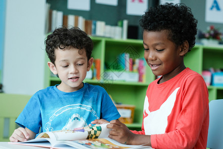 同班可爱的白色在室内美国人和非洲男孩在幼儿园课堂童教育和多样概念中一起阅读并快乐地学生们的习和阅读与背景
