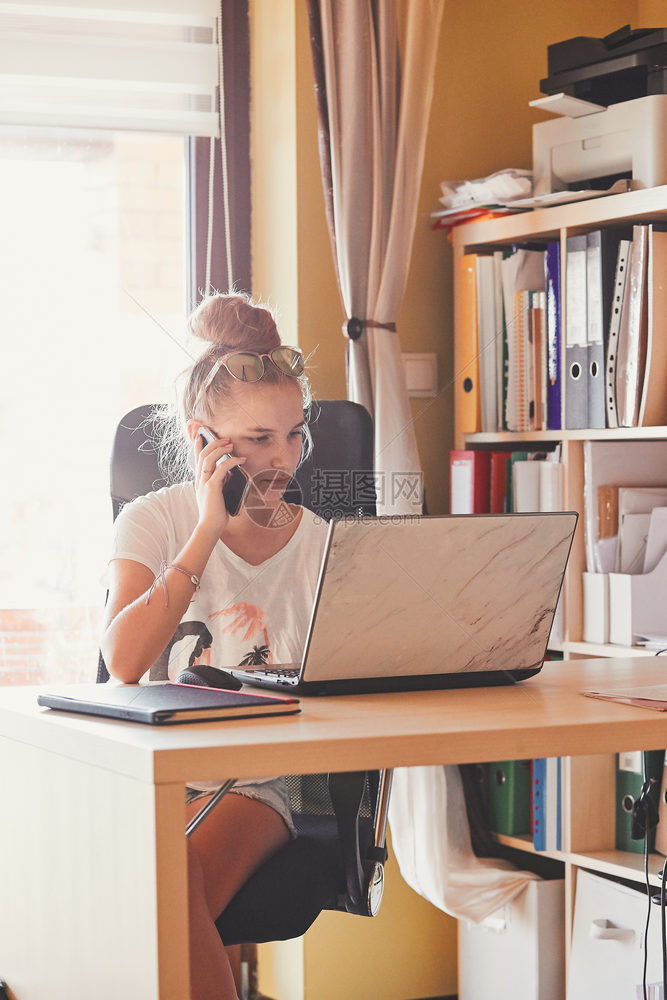 在家工作使用便携式计算机坐在家庭办公室桌前的年轻妇女Candid人真实时刻情况等忙碌的互联网在职图片