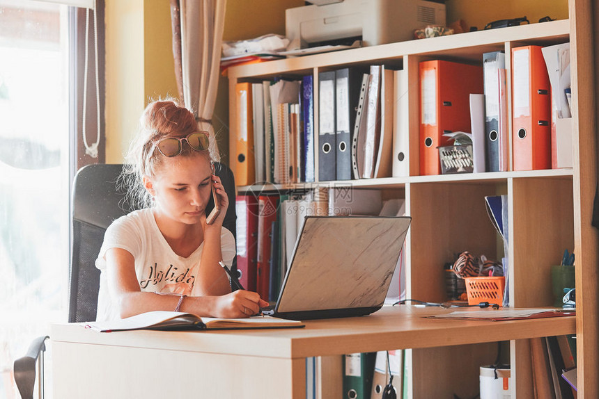 坐着现代的在家工作使用便携式计算机坐在家庭办公室桌前的年轻妇女Candid人真实时刻情况等复制图片