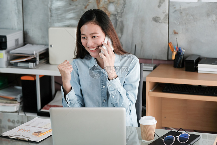 胜利年轻的亚洲女商人在办公桌工作时用微笑的面脸说话讲电和手举起来商业概念取得成功桌子人们图片
