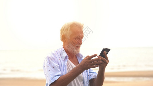 在海滩上通过手机微笑的老人长者短信息放松移动的白种人图片
