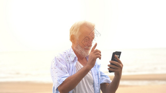 在海滩上通过手机微笑的老人长者短信息陈年男人技术图片