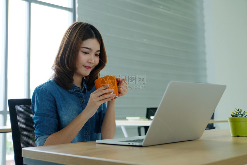年轻的亚洲女用微笑的面容工作桌背景的积极情绪临时办公室生活在家工作的概念等咖啡杯相聚的年轻女手笔记本电脑泰国图片