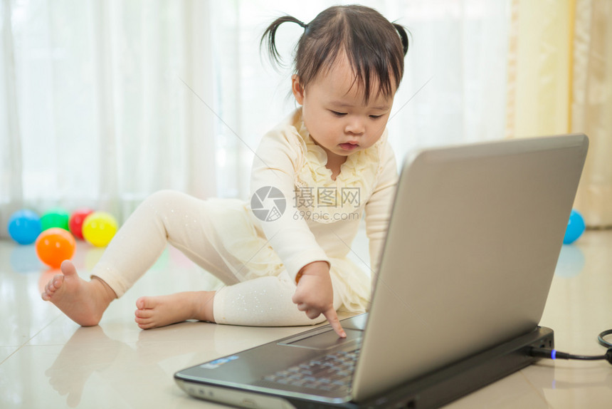 互联网小亚洲女孩在家里玩笔记本电脑的肖像婴儿监视器图片