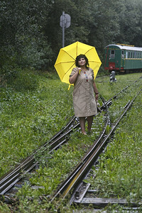 积极的妇女站在铁路轨上在雨季夏日扶着黄色雨伞女士夏天图片