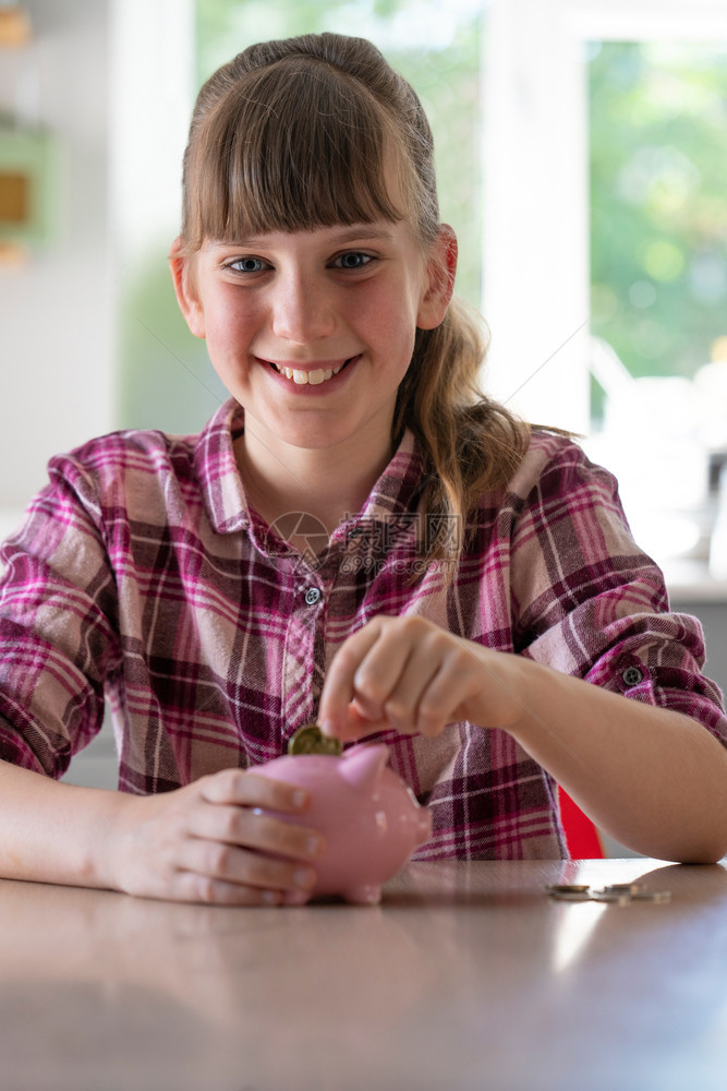 童年将硬币放进小猪银行的女童肖像在家中展示储蓄资金快乐的女孩们图片