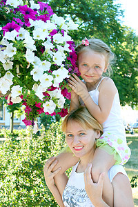 人们女儿坐在她母亲的旁边在市公园里放着许多花朵微笑图片