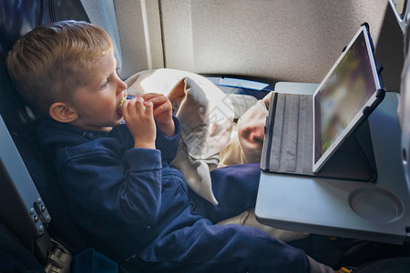 男孩坐在飞机上吃饭看平板电脑背景图片