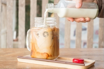 挤牛奶到冰的咖啡杯股票照片屋木制的冰镇图片