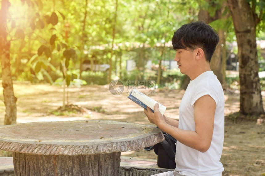 大学坐着春天在公园长凳上读书的年轻放松男子图片