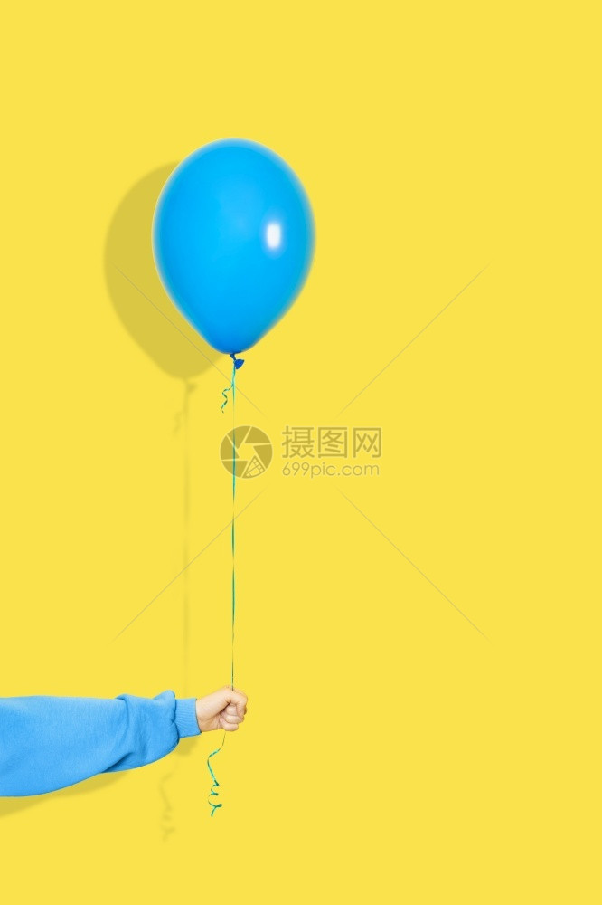 飞行庆典或者女手持蓝色气球派对或呈现概念蓝色气球并手上连帽衫隔离在黄色背景上女手持蓝色气球派对或呈现概念蓝色气球并手上连帽衫隔离图片