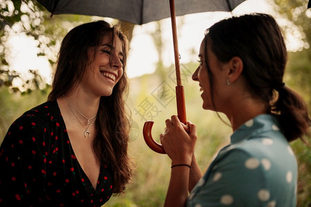 两名年轻妇女在田地上拿着雨伞站在身裙子和运动鞋的树丛中站立爱白天树木背景图片
