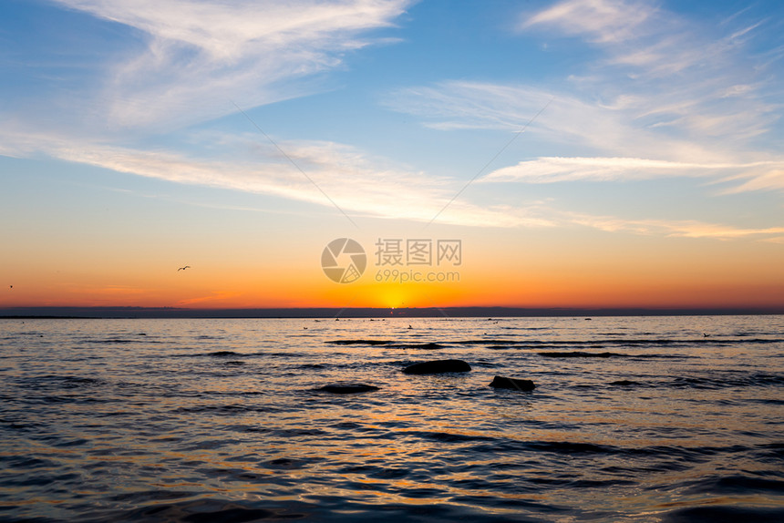 橙风景优美明亮的天空鸟类岩石和海水在面日落反射图片