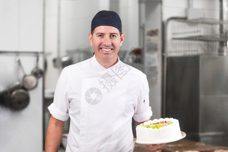 年轻的服务微笑糕点厨师在店房里展示蛋糕微笑的点厨师展示蛋专业的背景图片