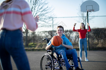 积极的男女玩篮球和朋友一起打篮球的轮椅男少年孩图片