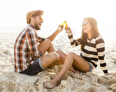 吐司假期在海滩上玩乐笑和喝啤酒的年轻夫妇太阳镜图片