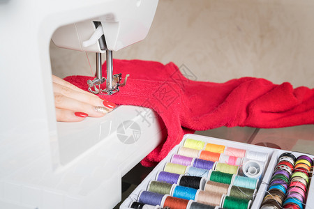 手时尚缝纫机上的女青年缝纫织物在涂上彩色池子阶段的缝合过程红色的图片