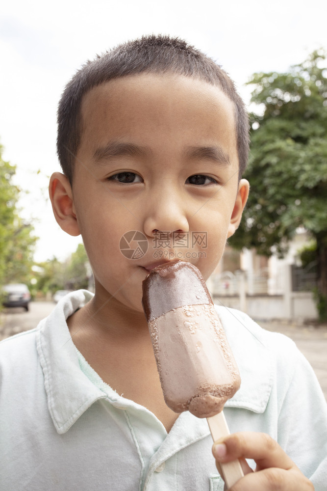 快乐的奶油近距离面对亚洲男孩吃巧克力冰淇淋和快乐面孔童年图片