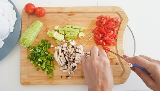 里万切拉斯素食主义者帕利卡拉斯石板在木切上用砍手和切蔬菜割板上的顶部视图背景
