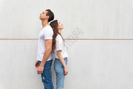 年轻快乐的一对情侣靠背站在白色城墙边女士爱愉快图片