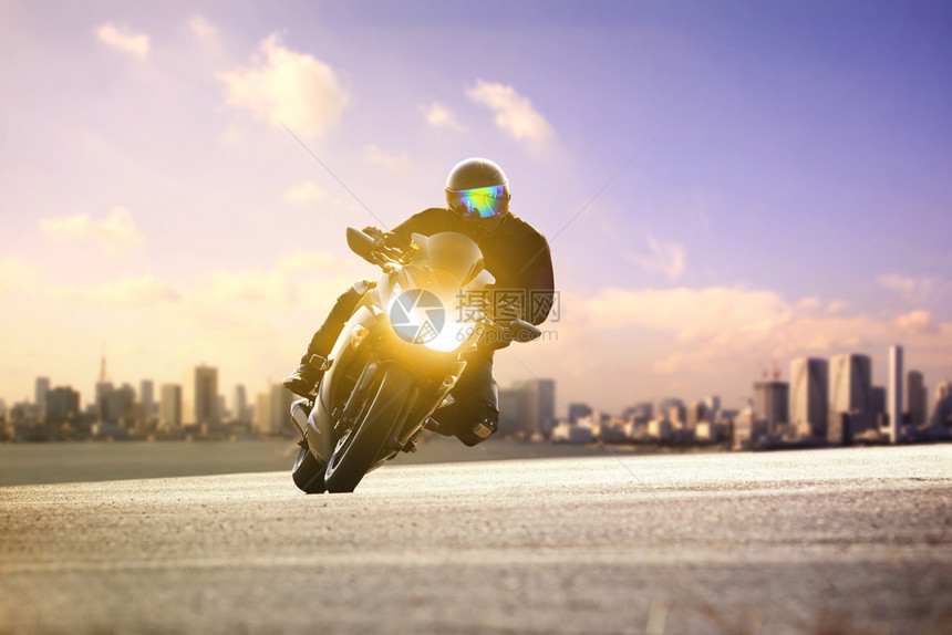 城市的沥青头盔男骑着运动摩托车在城市天线背景的弯曲路上倾斜图片