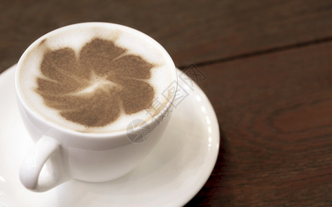 木制桌地板白陶瓷杯中卡布奇诺拿铁艺术的紧贴花朵模式喝饮料白色的图片