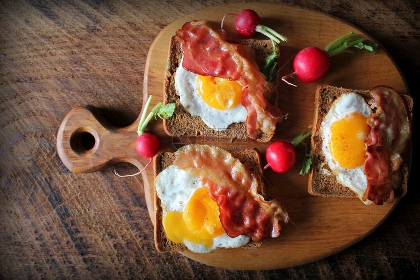 乡村煮熟的烤培根炸鸡蛋和面包三明治早餐在切菜板上吃煮餐桌烤培肉煎鸡蛋和面包三明治早餐在切菜板上吃木图片