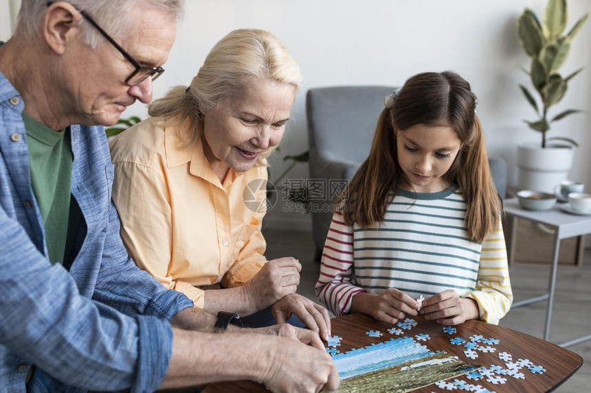 男在室内祖父母女孩玩拼谜游戏桌子图片