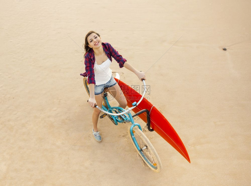 人们年轻的冲浪女子骑自行车在海滩上放松图片