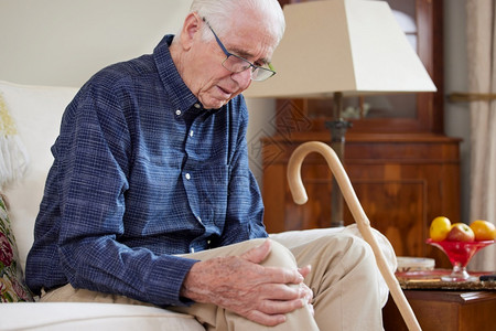 无效坐在索法家中的高级男子与因关节炎而受膝腿疼痛的家庭高级保持联合背景