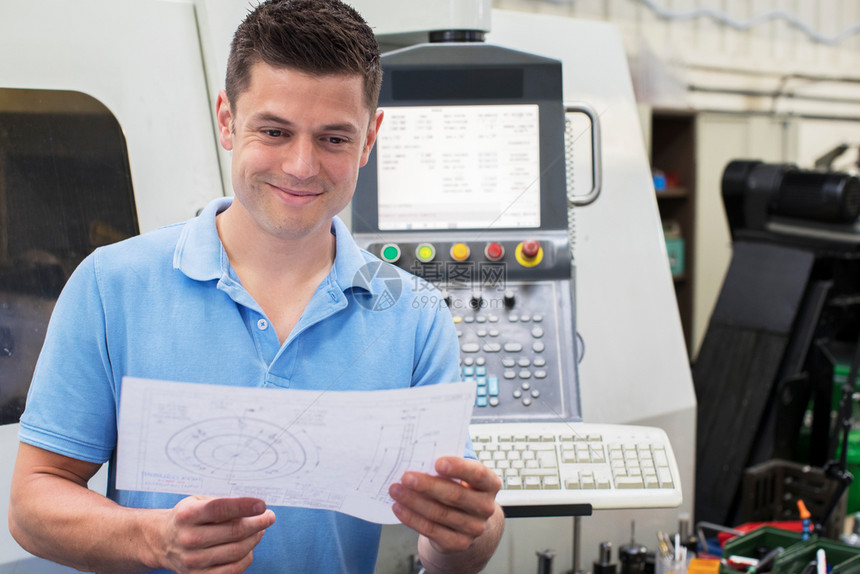 水平的制造业男工程师厂内具有技术绘图操作的CNC机器商业图片