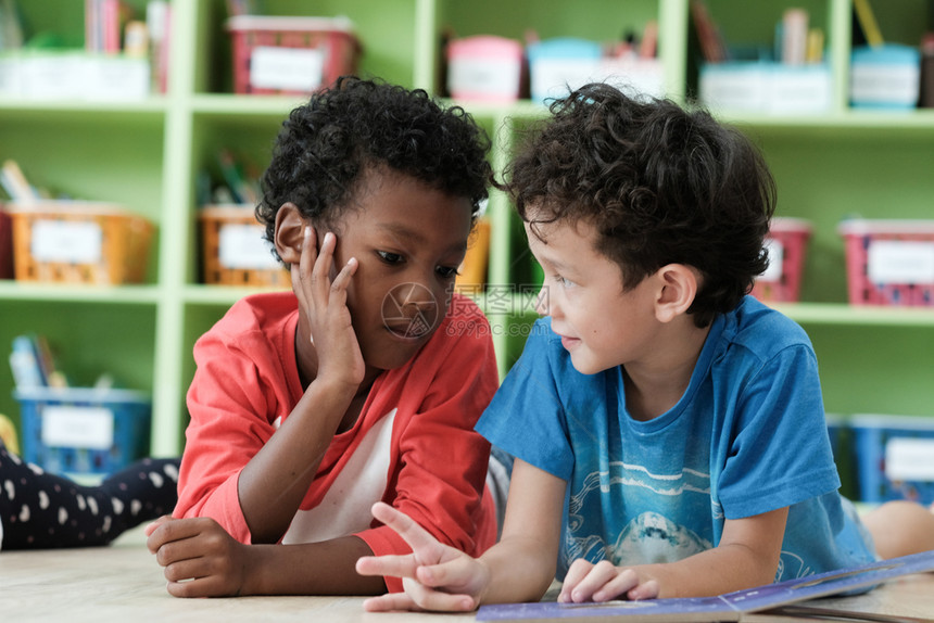 孩子们泰国美人和非洲男孩在幼儿园课堂童教育和多样概念中一起阅读并快乐地学生们的习和阅读与图片