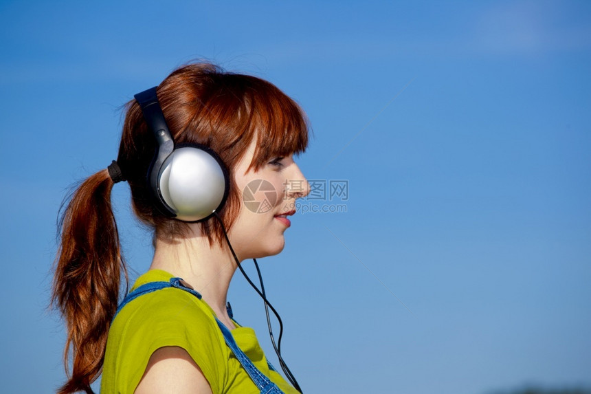 一种微笑位快乐女人的肖像在美丽蓝天上聆听音乐女孩图片