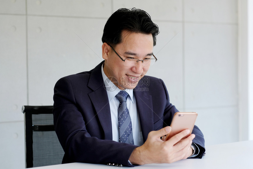 公司的成熟手机亚洲商人在办公室背景使用智能电话利商业和技术的务人员亚洲以办公背景使用智能电话图片