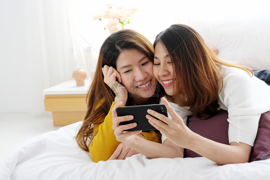 使用智能电话在家里快乐地使用智能电话Igbt夫妇生活方式的年轻可爱女夫妇屋年轻的感图片