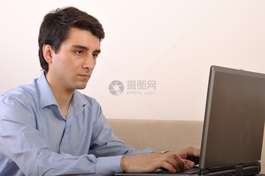 颜色男人屋在家沙发上坐着膝型电脑的有吸引力年轻人图片