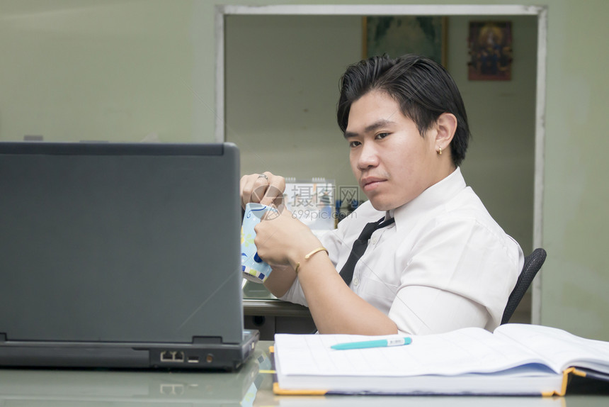商业迷惑年轻的亚洲商人在办公室用咖啡杯看笔记本电脑工作图片