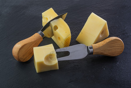 瑞士人小吃黄色的黑石板上三块奶酪用刀叉和图片