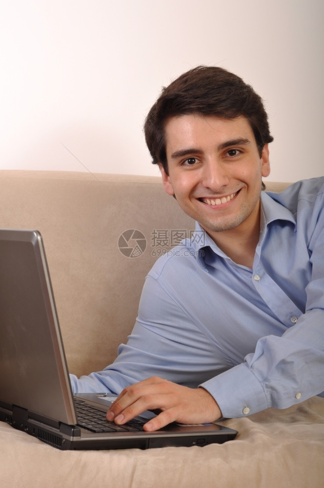 互联网个人电脑在家沙发上躺着膝型电脑的有吸引力年轻人男图片